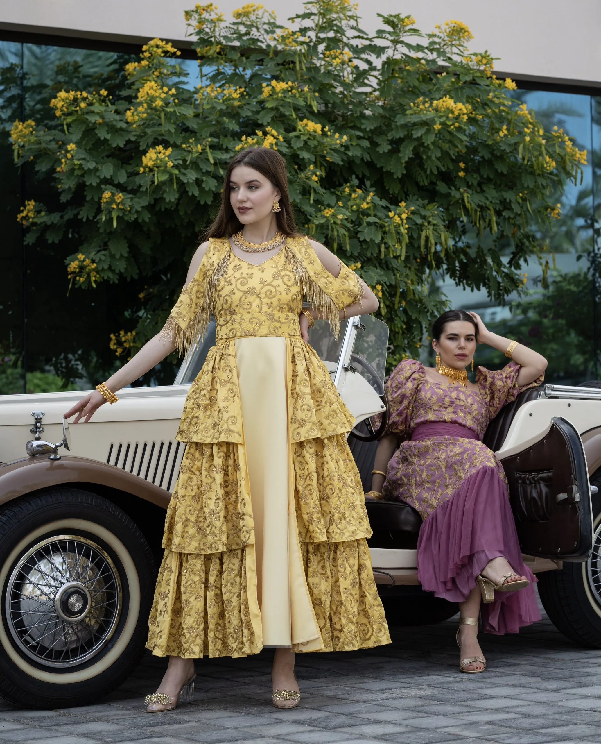 Women in gold dresses beside a vintage car