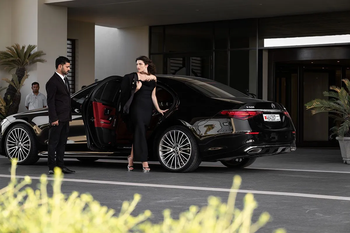 Woman in an evening dress beside a black sedan at night