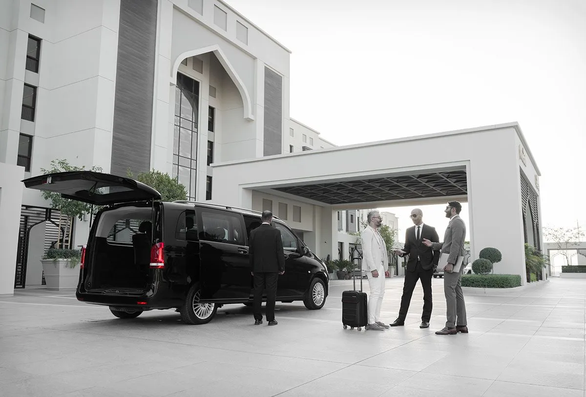 Chauffeur loading luggage into a black van outside a villa