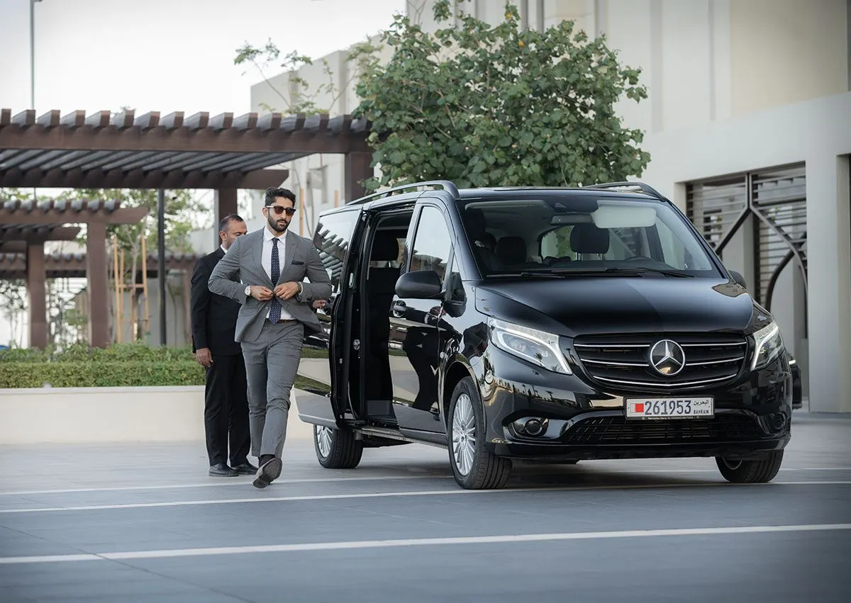 Man in a suit beside a black van under palms
