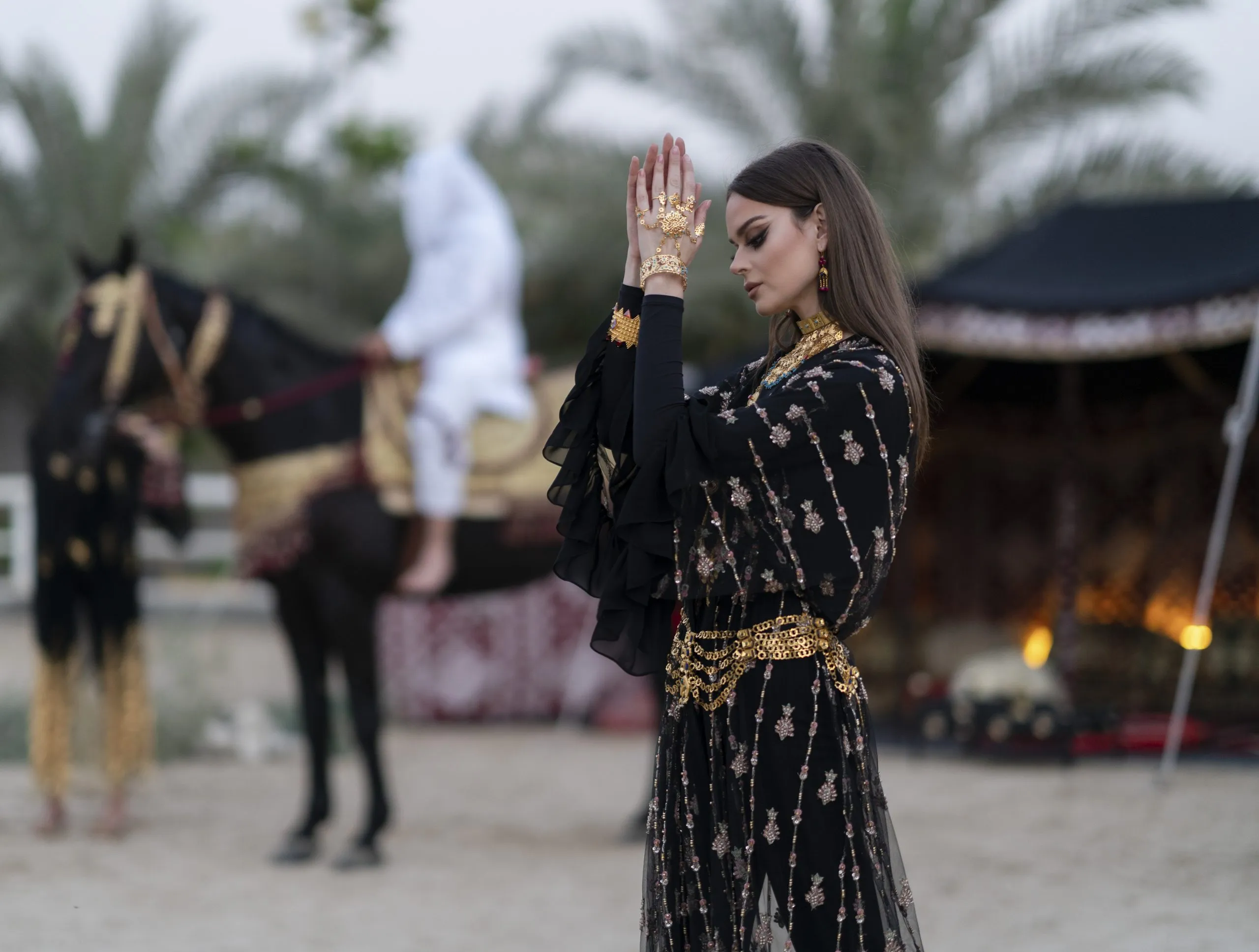 Woman in an embroidered abaya with henna, horse behind her in the desert