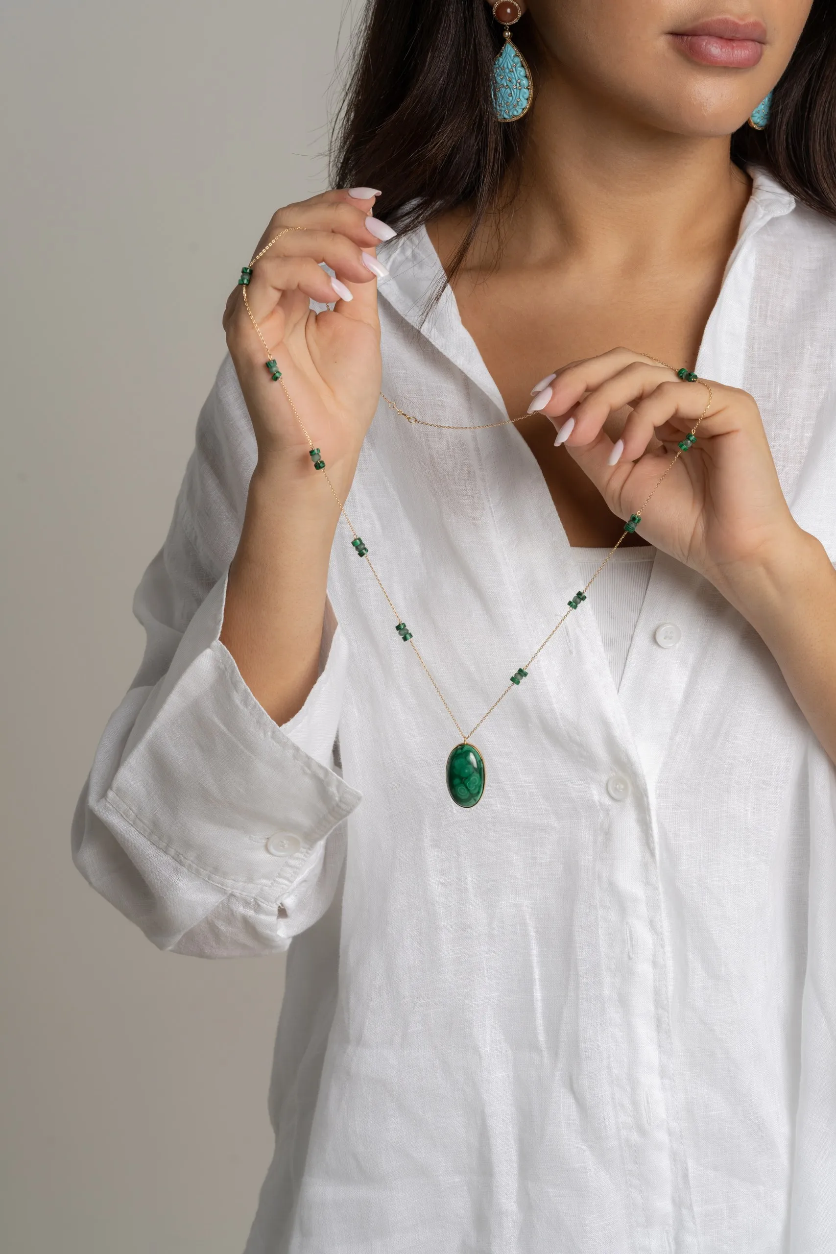 Woman in white holding a green gemstone pendant