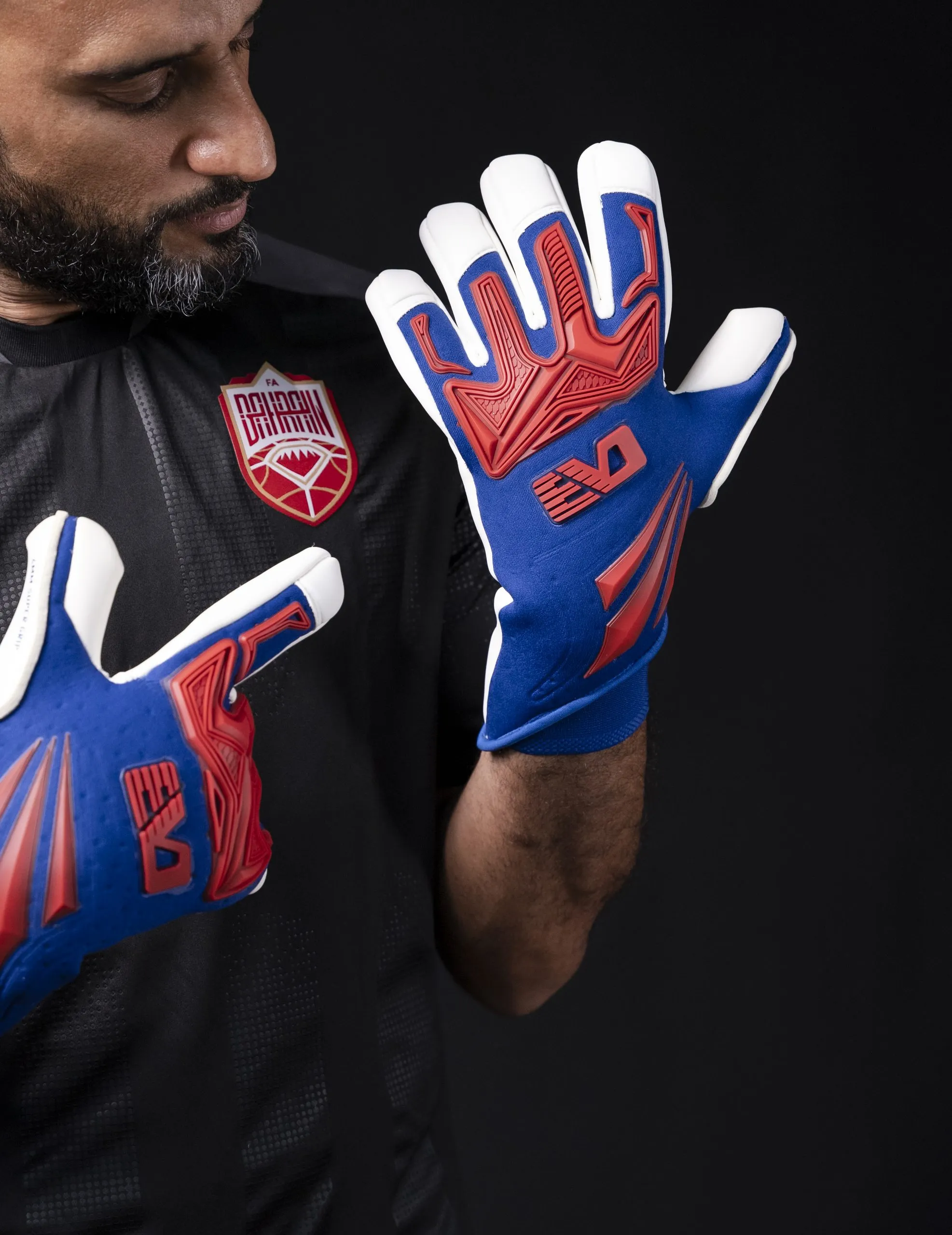 Man in sports kit wearing red and blue goalkeeper gloves
