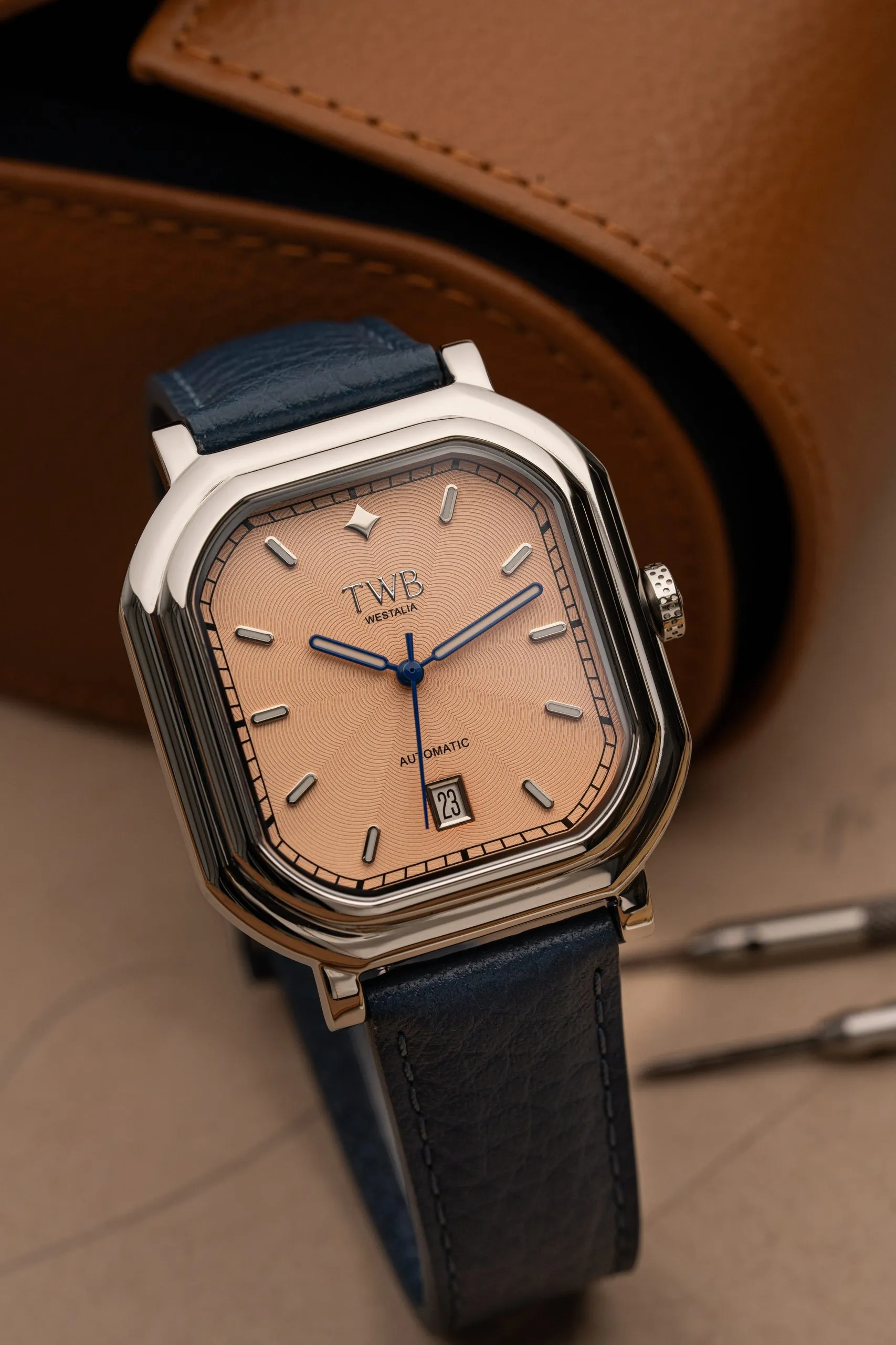 Watch with a blue leather strap on a tan leather surface