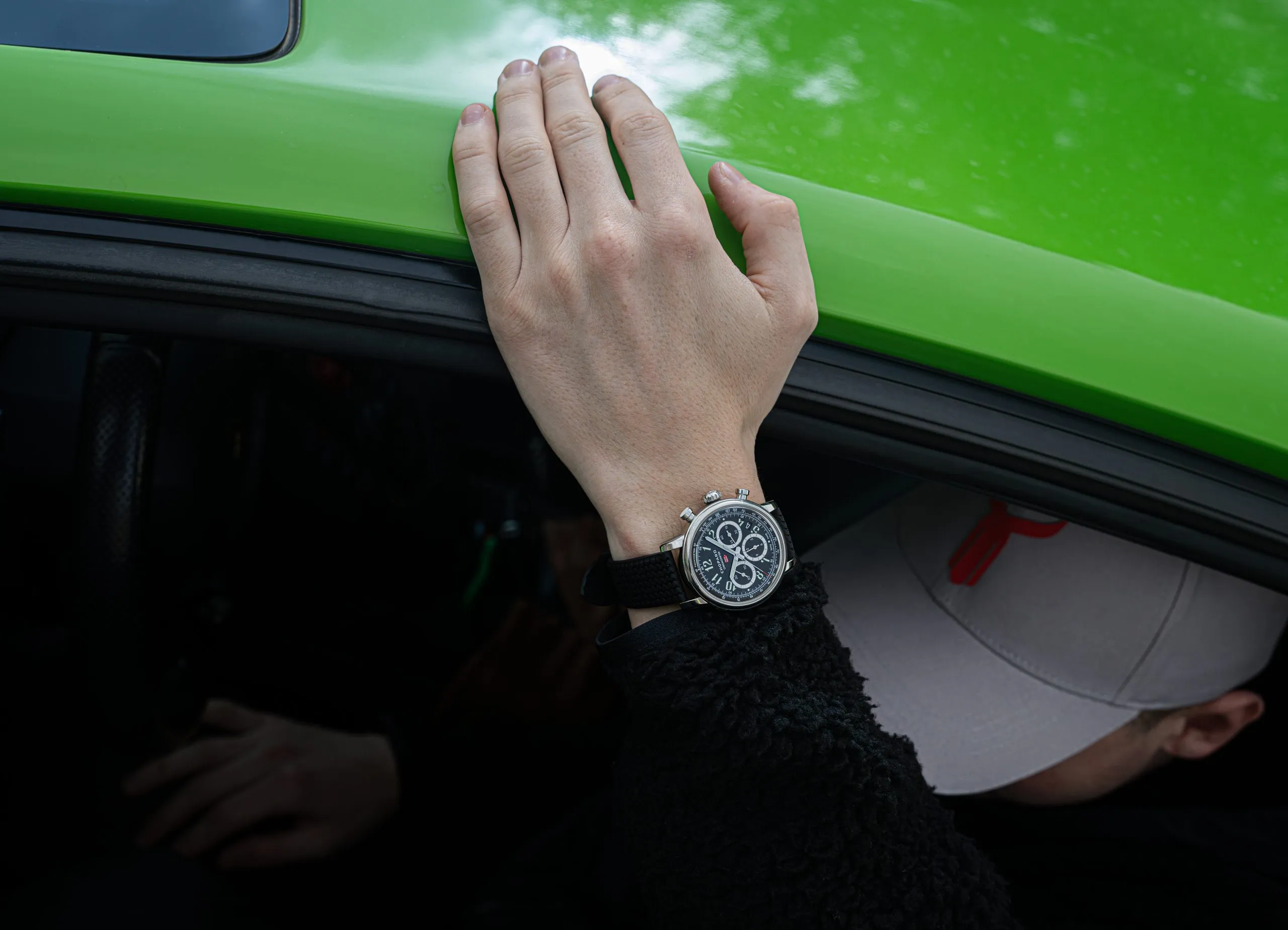 Watch on a wrist resting on the door of a green supercar