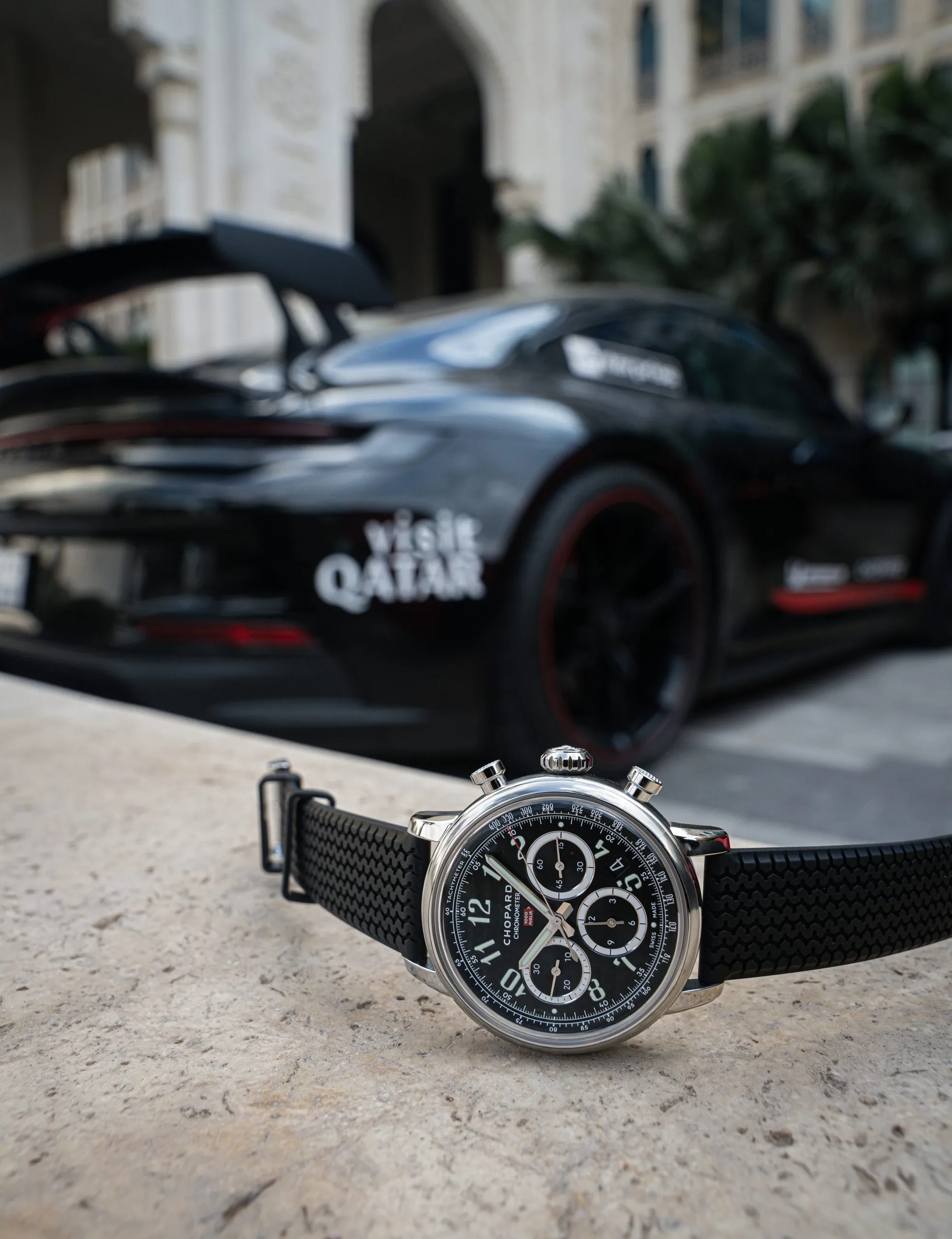Chronograph in the foreground with a black supercar behind
