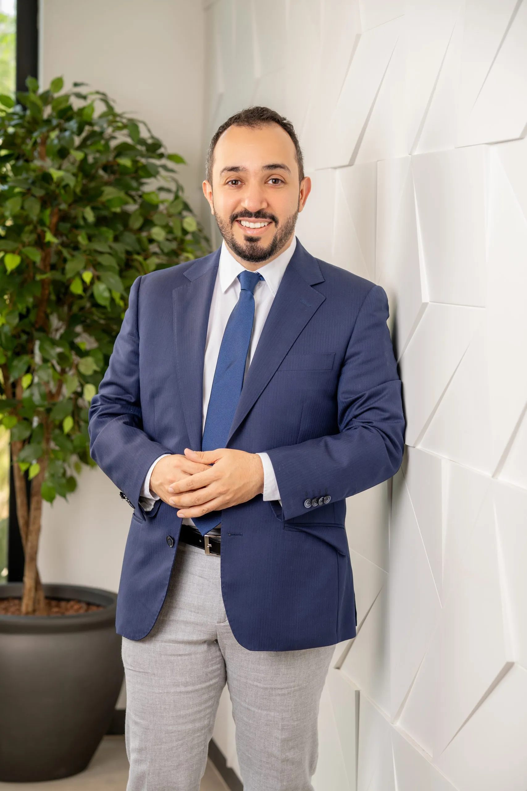 Bearded man in a blue blazer beside an indoor plant