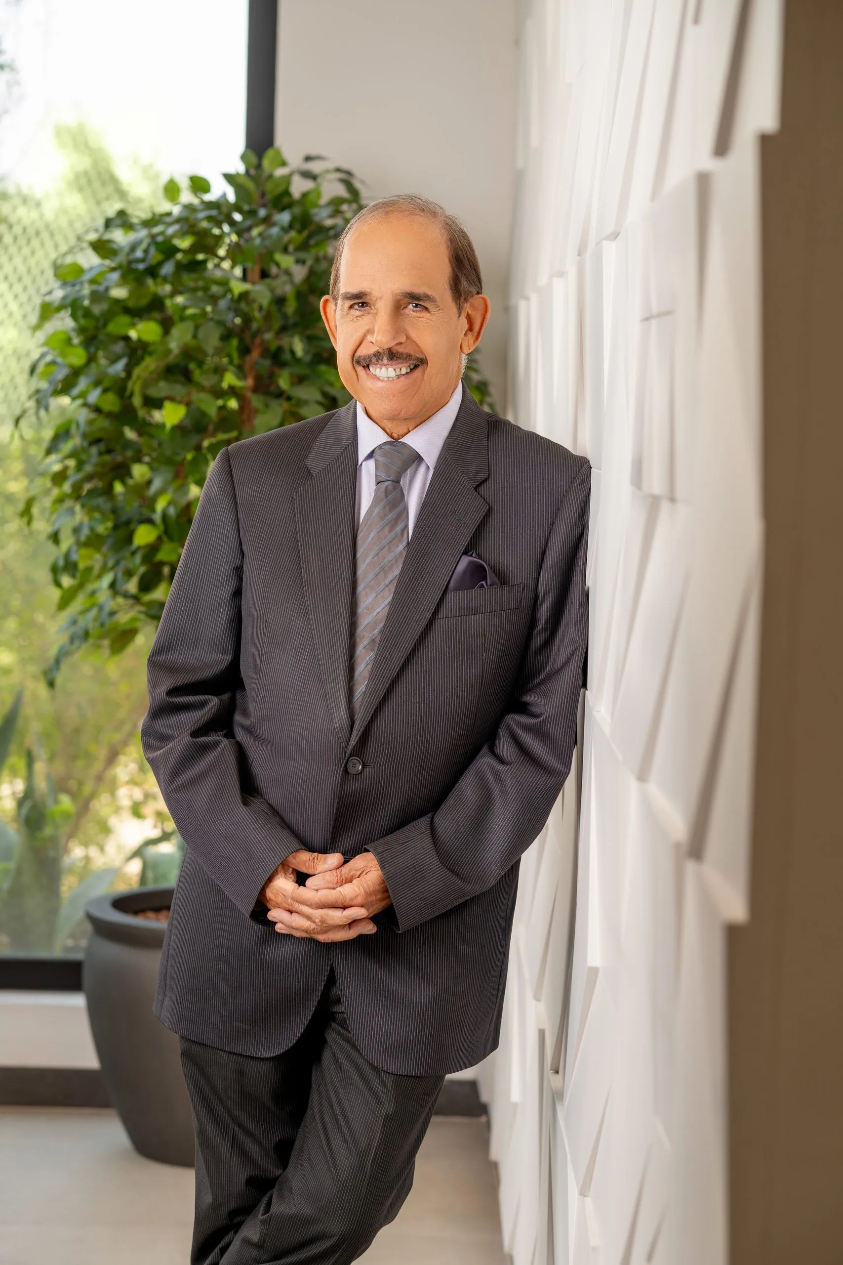 Senior doctor in a suit standing by a planted wall